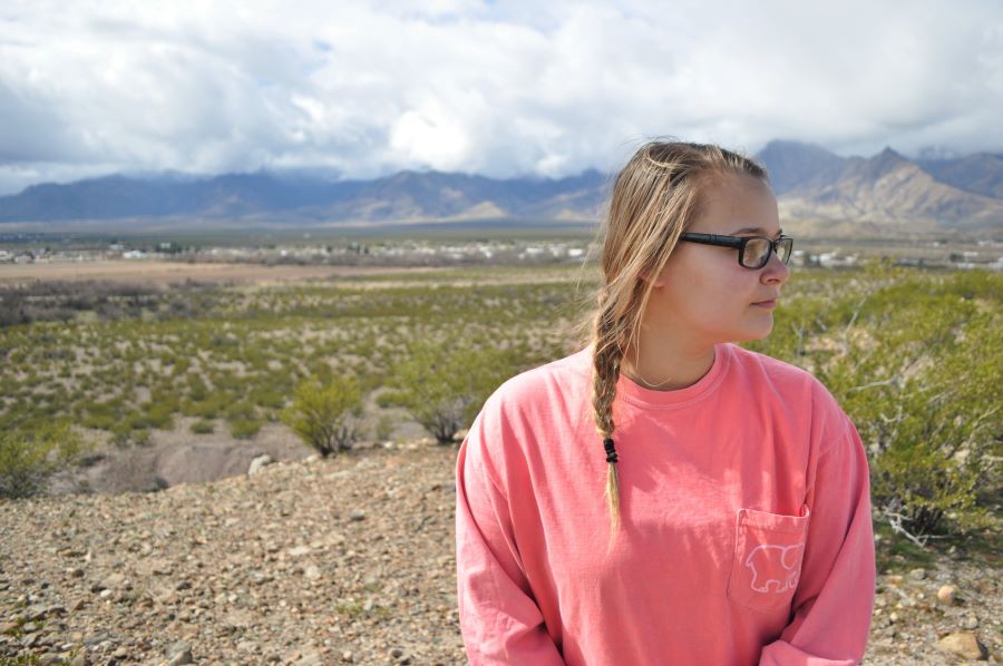 portrait of a young woman, wearing pink, posed in front of a natural desert background