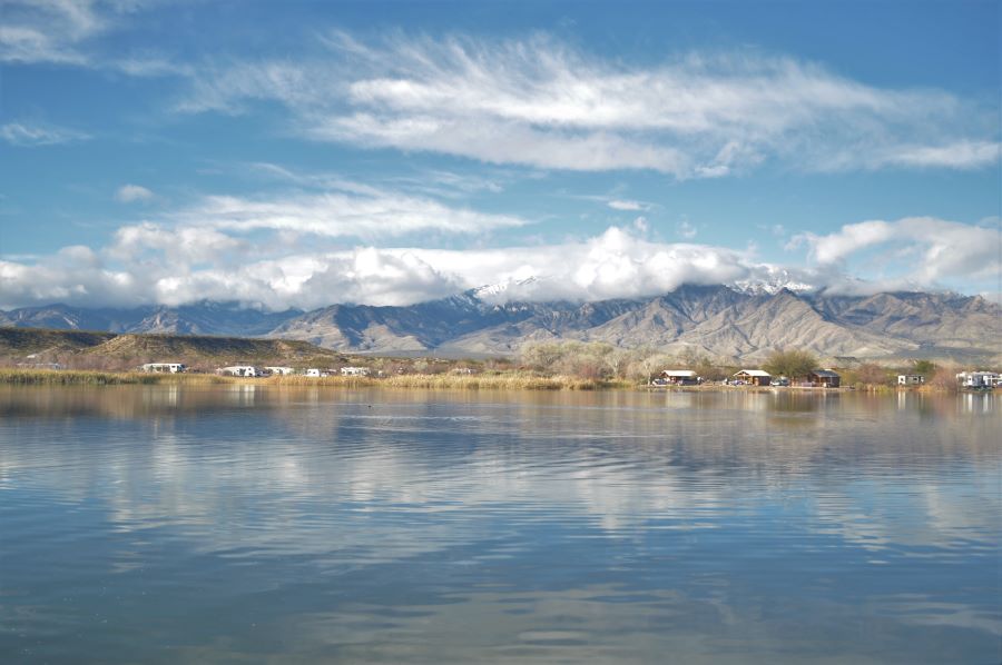 A landscape photo featuring a lake in the foreground and a cloud covered mountain top in the background.